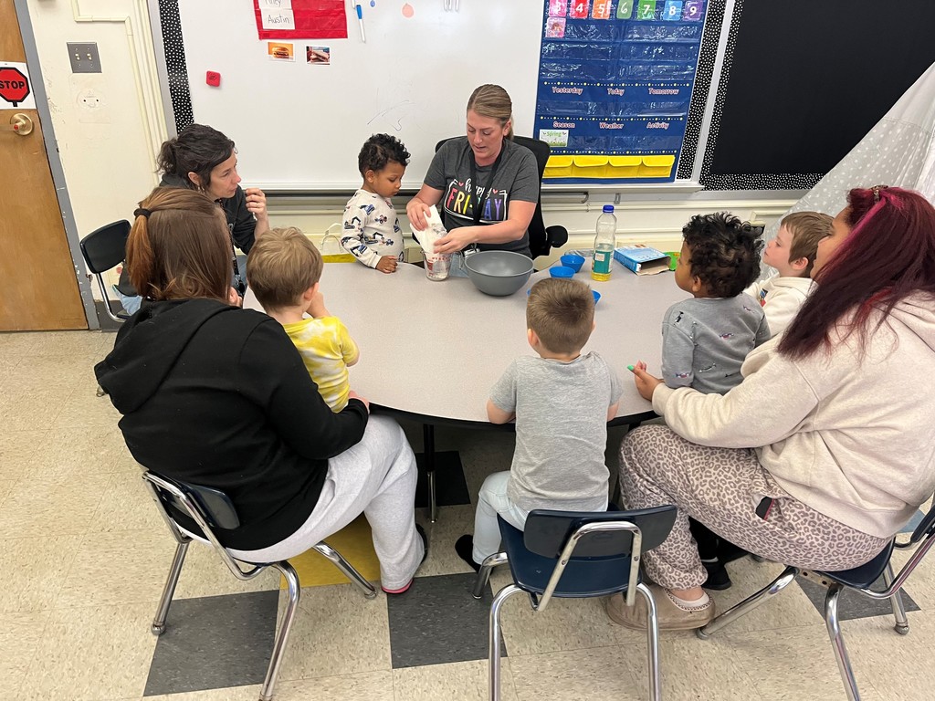 students and adults watching a teacher help a student with ingredients for cupcakes