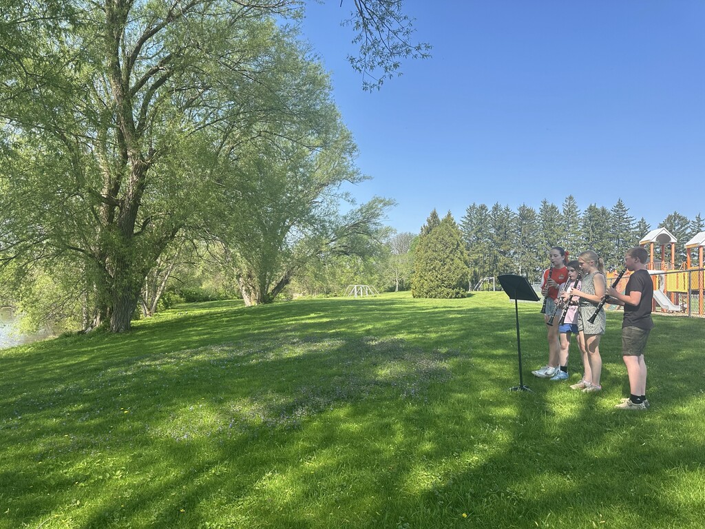 three students playing clarinets outside