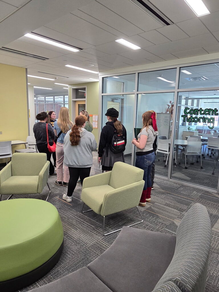 students standing in a room at college listening to a speaker