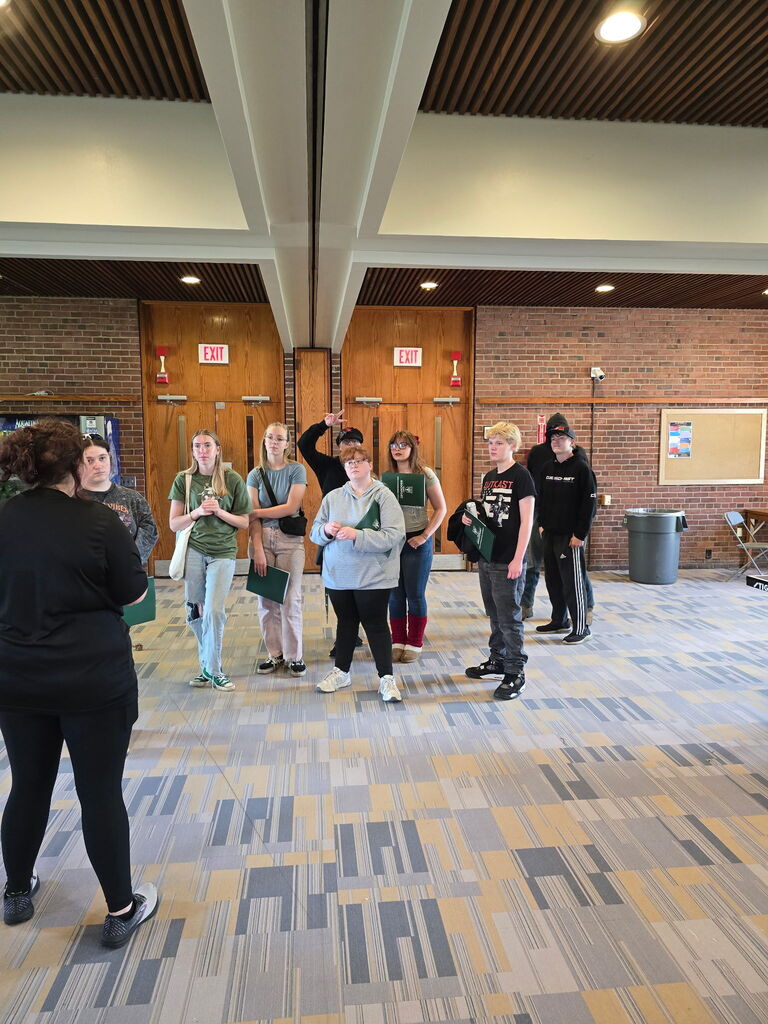 students standing in a college entrance listening to a speaker