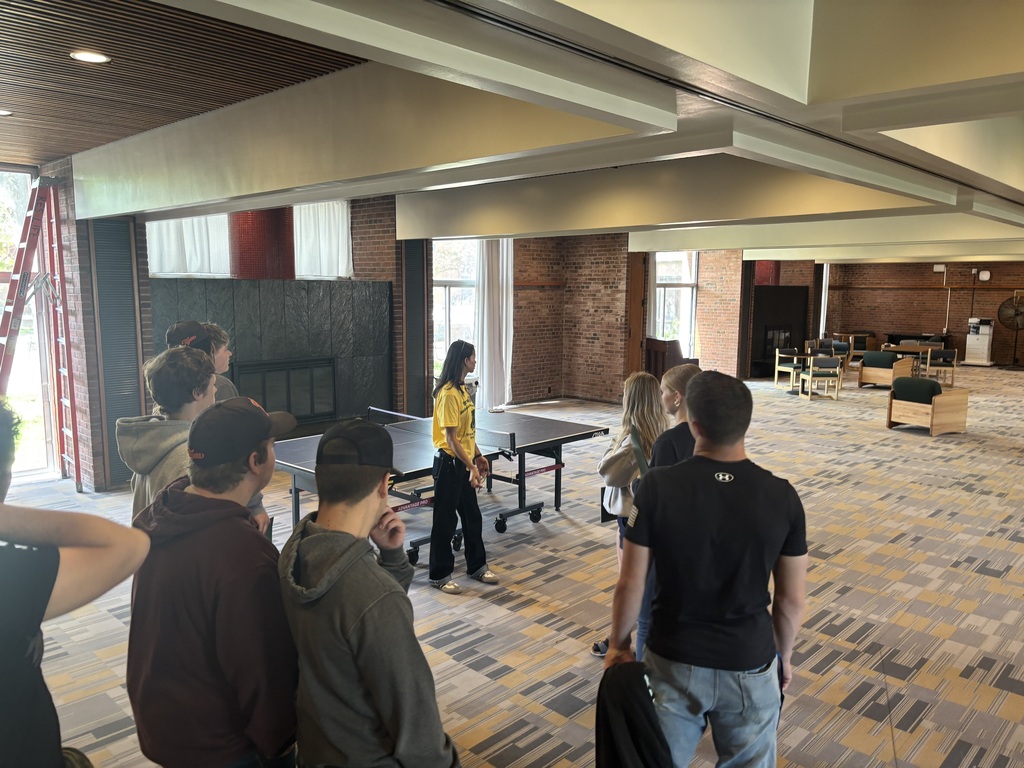 students standing in a room at college listening to a speaker