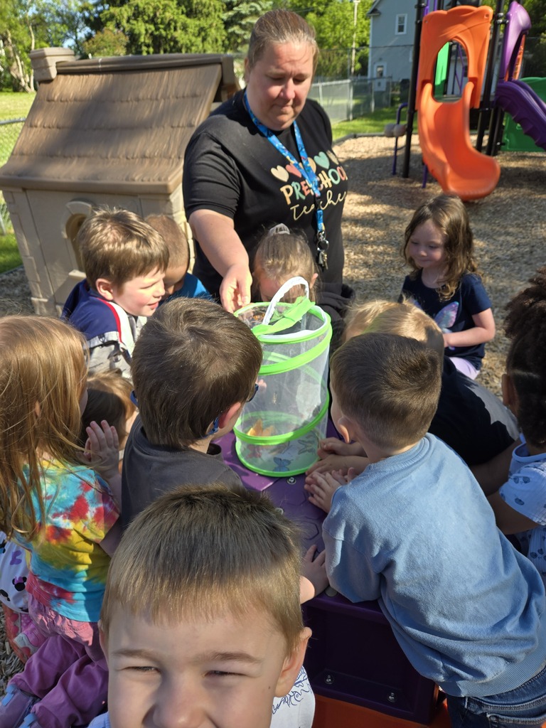 teacher holding butterfly container while students gather around it