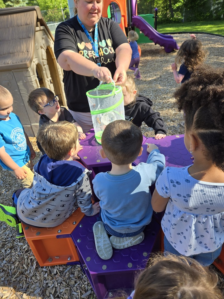 teacher holding butterfly container while students cluster around to observe it