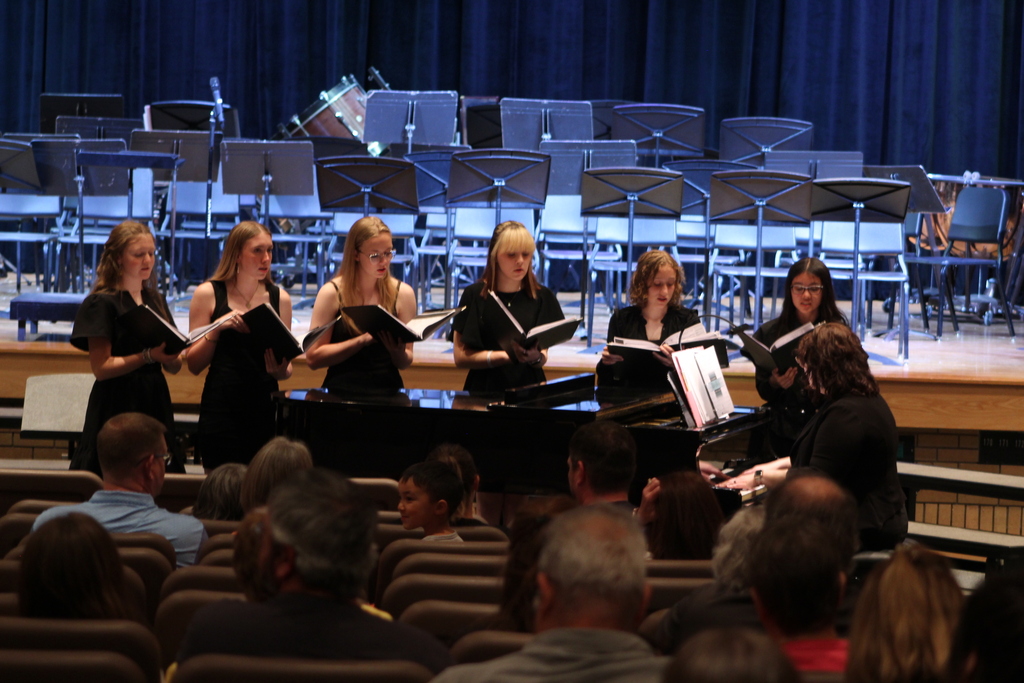 select choir members singing around piano