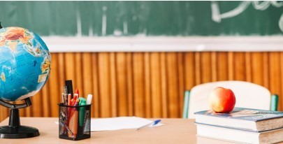 Image of a teacher's desk with a globe, pens, text books and an apple. with a blackboard in the background.