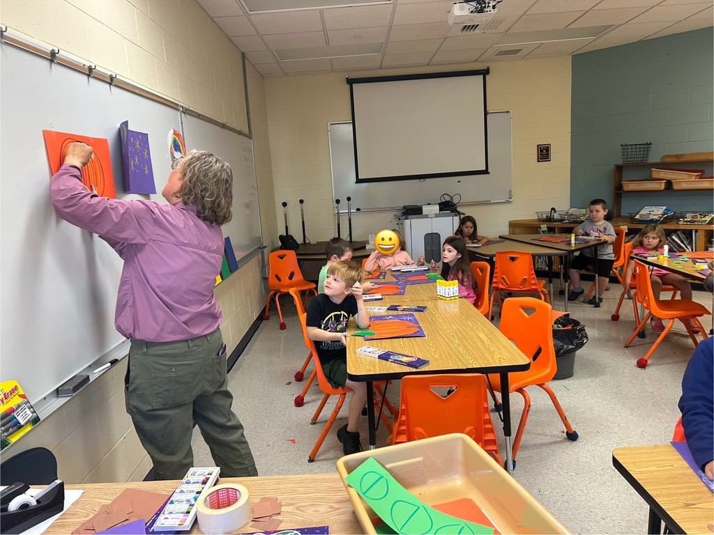 This picture shows a student working on an art project. A cut out of an orange pumpkin on a purple background.