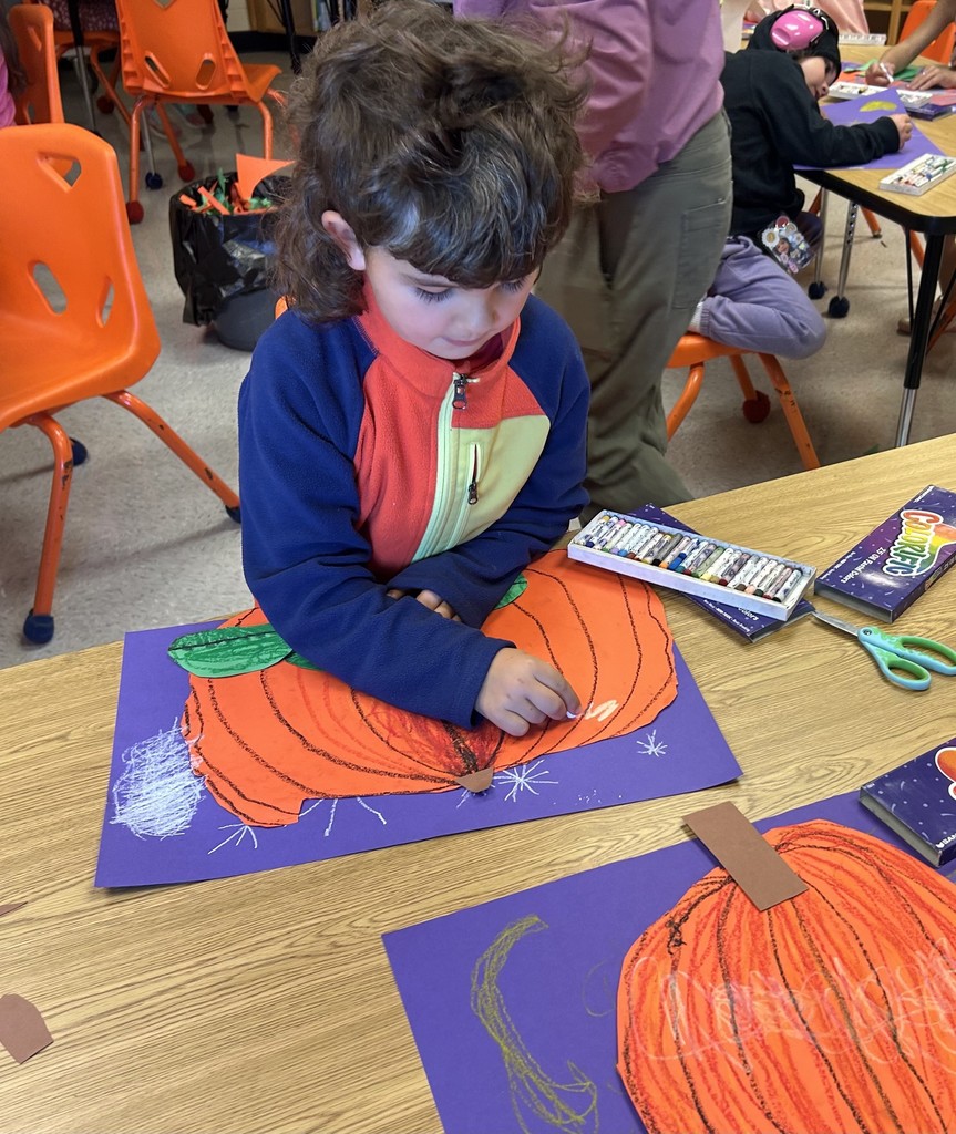 This picture shows a student working on an art project. A cut out of an orange pumpkin on a purple background.