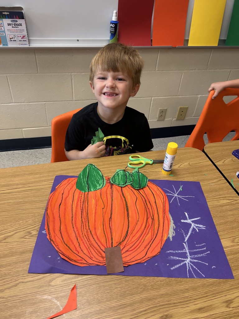 This picture shows a student working on an art project. A cut out of an orange pumpkin on a purple background.