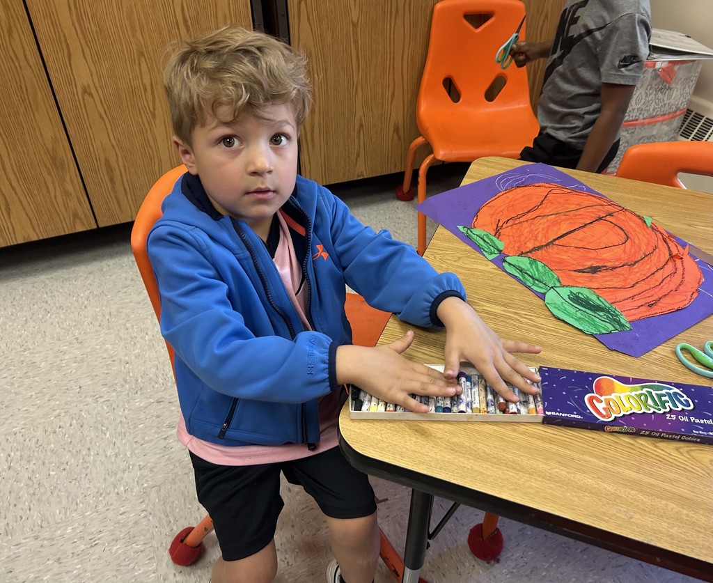 This picture shows a student working on an art project. A cut out of an orange pumpkin on a purple background.