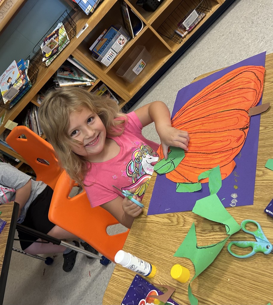 This picture shows a student working on an art project. A cut out of an orange pumpkin on a purple background.