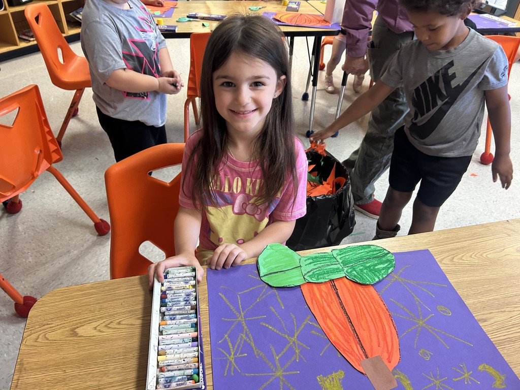 This picture shows a student working on an art project. A cut out of an orange pumpkin on a purple background.