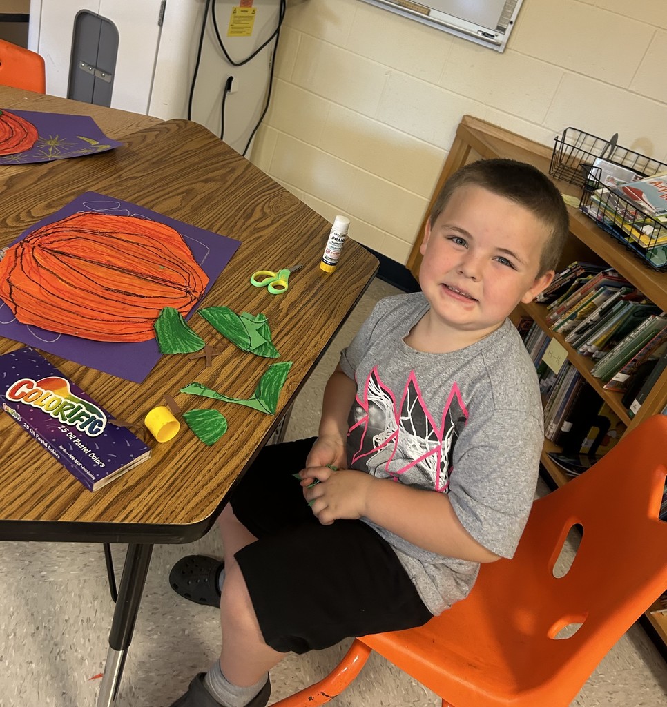 This picture shows a student working on an art project. A cut out of an orange pumpkin on a purple background.