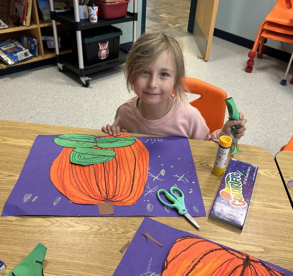 This picture shows a student working on an art project. A cut out of an orange pumpkin on a purple background.