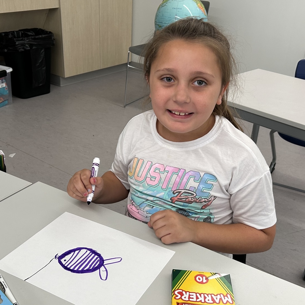 Female student drawing a fish on a box with a purple marker.