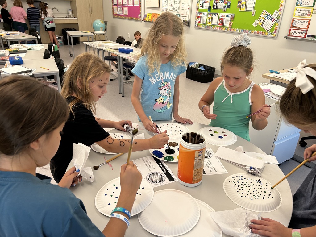 Five female students painting on the backs of paper plates.