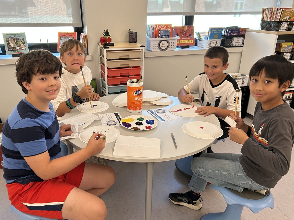 Four male studen ts painting paper plate backs.