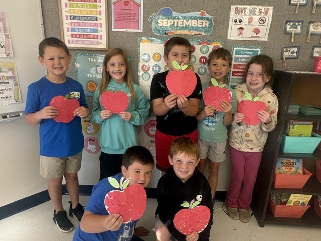 Seven students display their finished tear-art apples by holding them up.