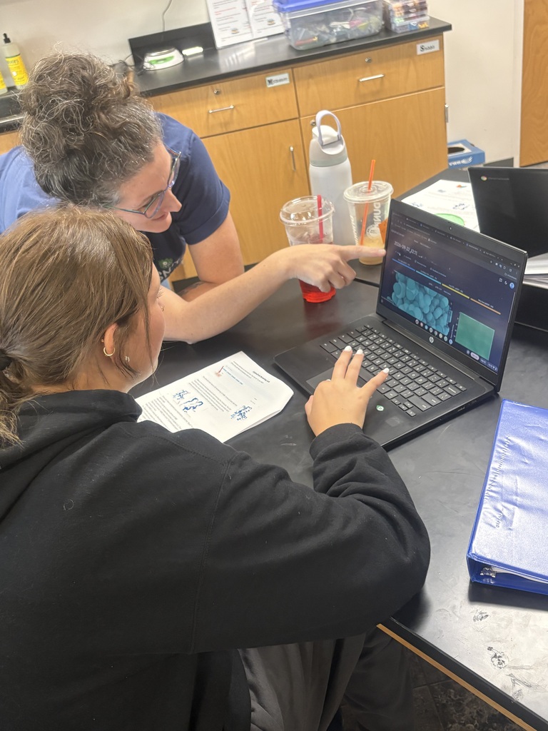 A teacher assits a femail student with virtual protein-folding software on her Chromebook.