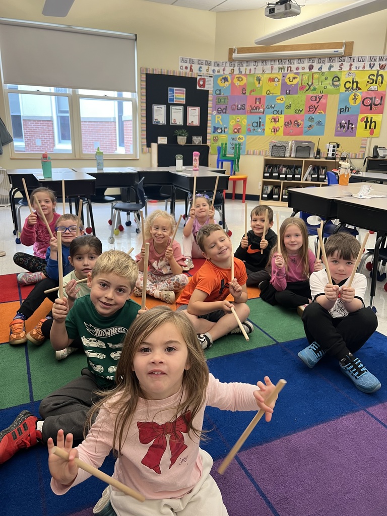 A group of students sit on a carpeted floor tapping out syllables with their phonics blocks.