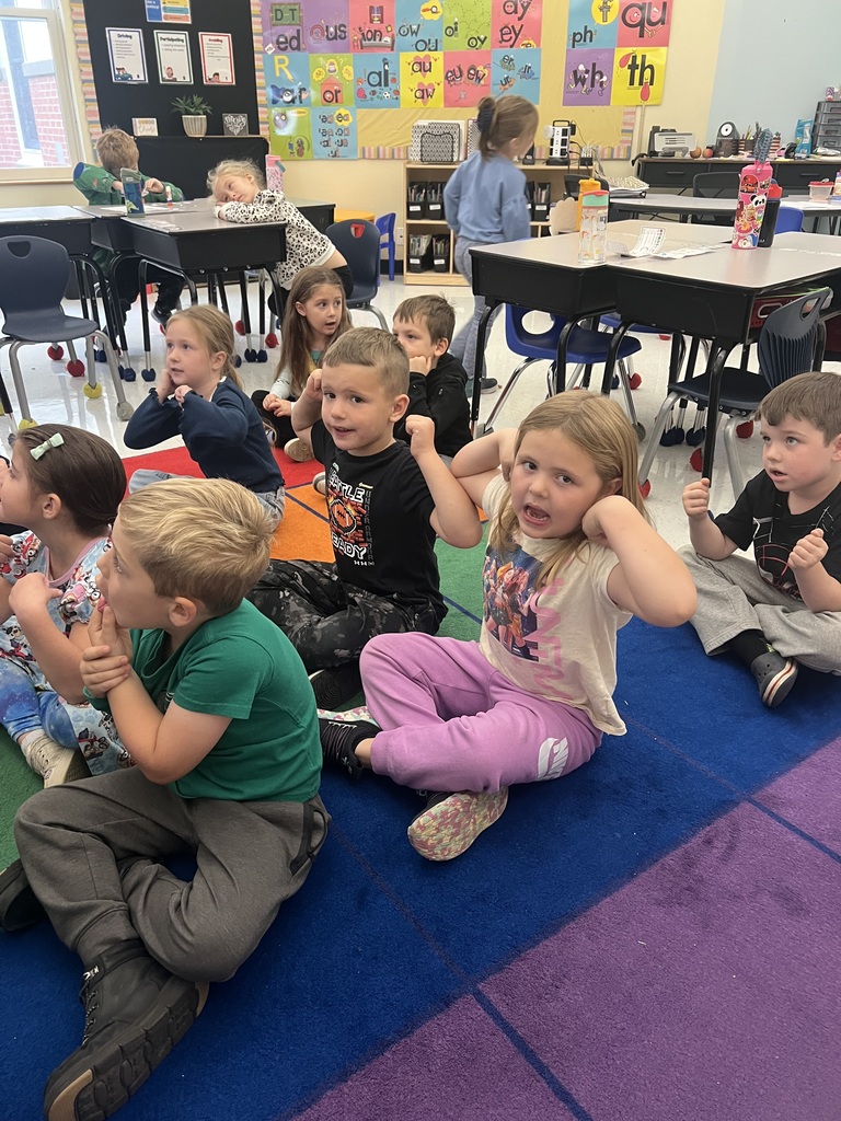 A group of students sit on a carpeted floor singing the "Better Alphabet Song".