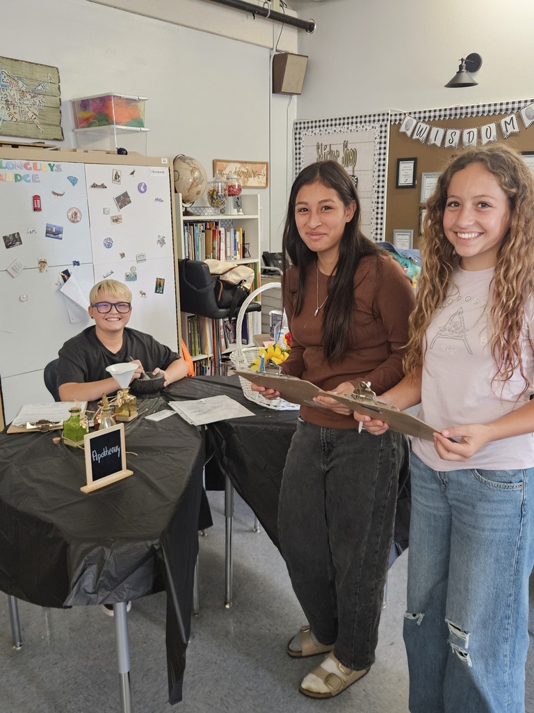 7th Grade Social Studies - learning about the Middle Colonies. Two female students with clipboards and a male student sitting behind a desk work on an activity.