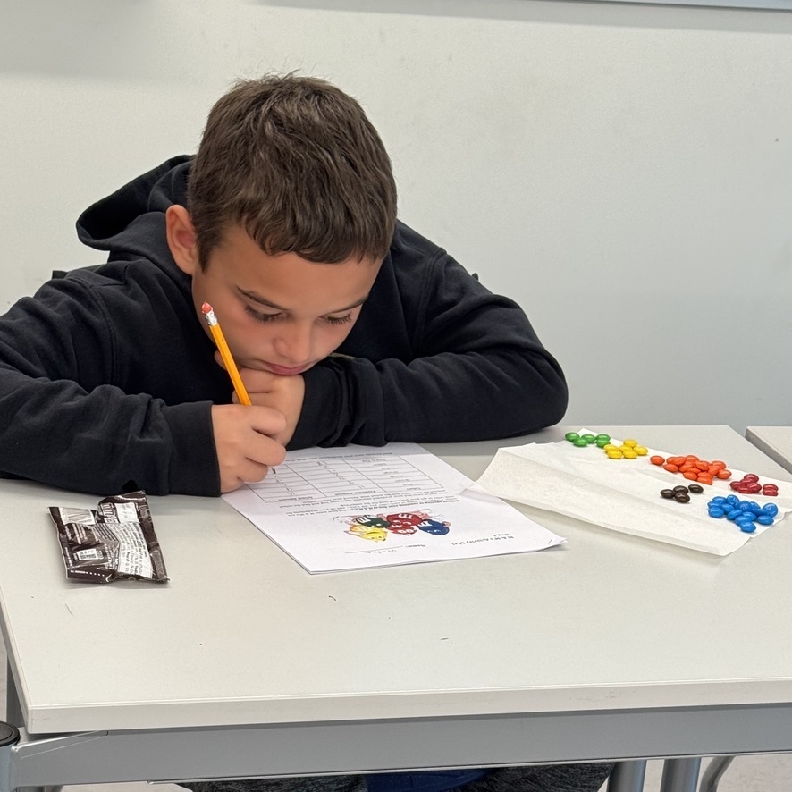 A young man studies a math worksheet that includes a number of M&Ms