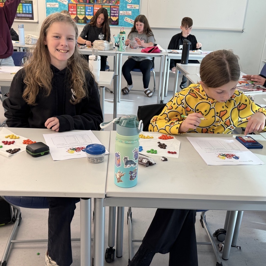 Two female students having fun working on their project, both have worksheets and piles of M&Ms