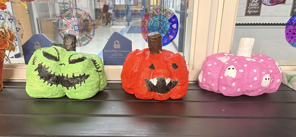 Three brightly colored paper mache pumpks, two jack-o-lanters one green and one orange and a pink one with white ghosts