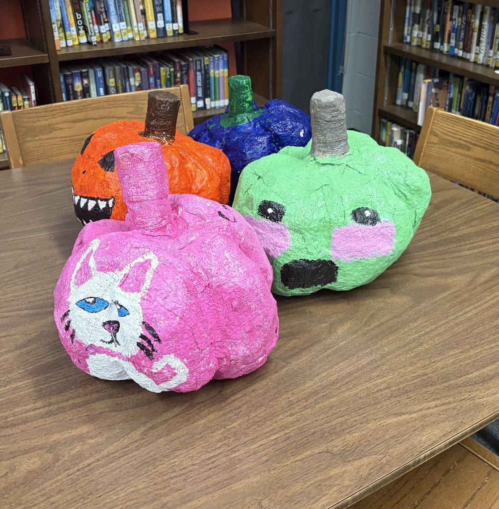 A group of four brightly colored paper mache pumpkins including a orange jack-o-lantern and a pink one featuring a white cat