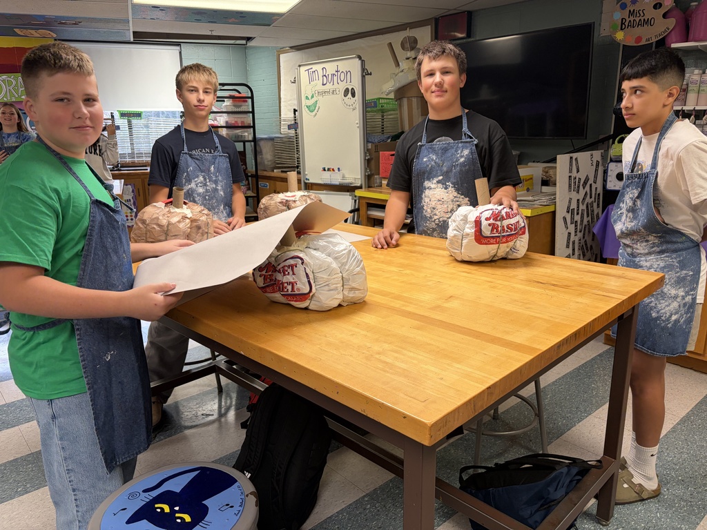 Four young men dressed in aprons prepare to make paper mache