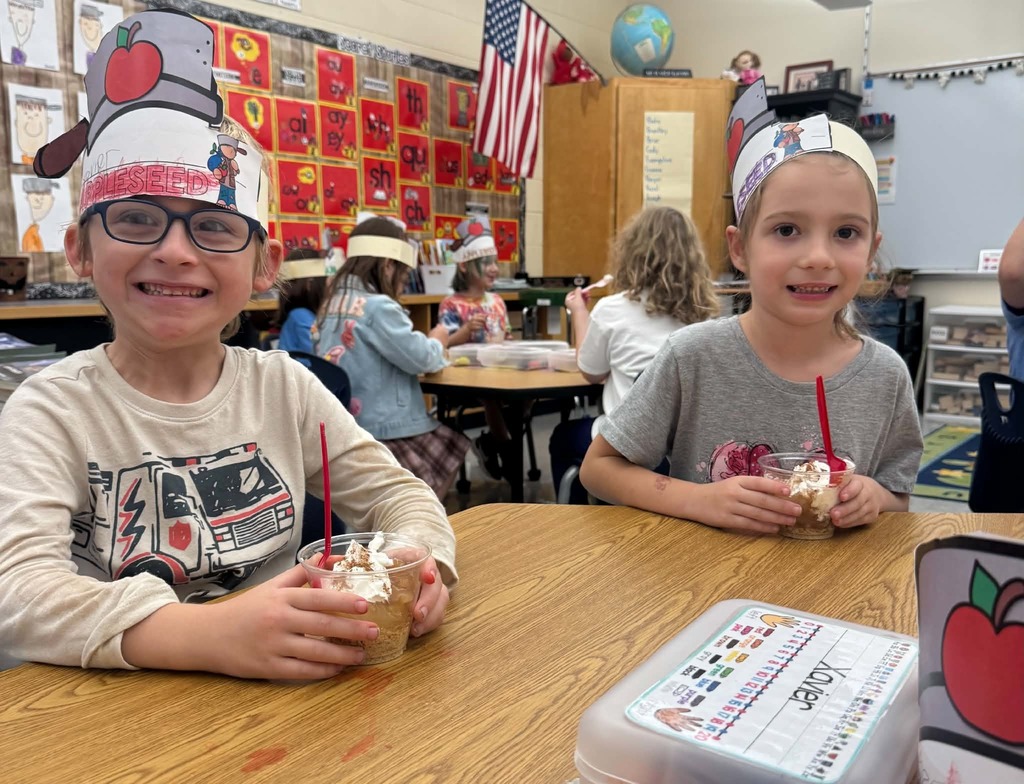 Two students, a male and female proudly wear their paper apple crowns while enjoing apple pie in a cup.