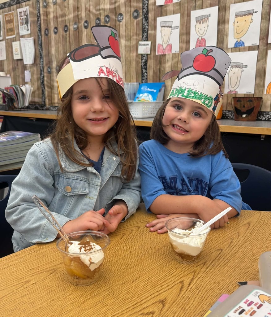 Two young ladies, wearing apple festooned paper crowns enjoy apple pie in  a cup.