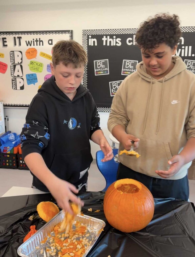 A young man holds a pumpkin lid while his team made scoops out innards..