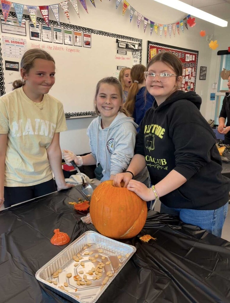 Three girls pose proudly behind their pupkin with a tray of seeds in the foreground.