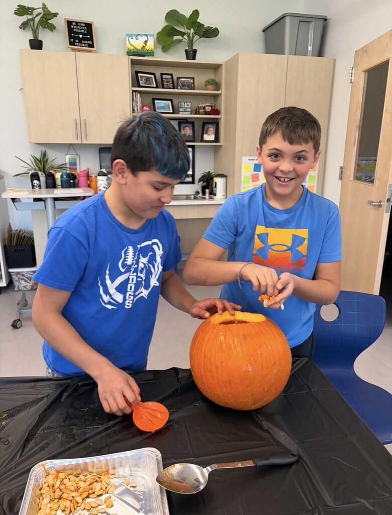Two excited young men disembowel a pumpkin.
