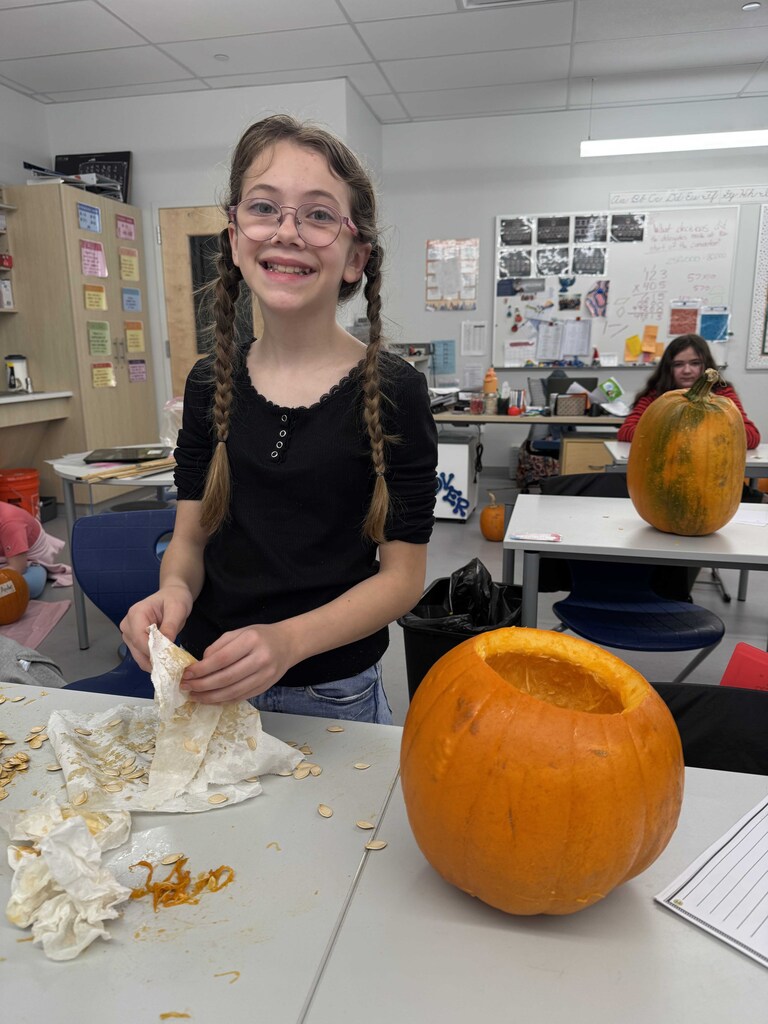 A smiling young lady with long braids stands behind her emptied pumpkin  cleaning her hands and work space.