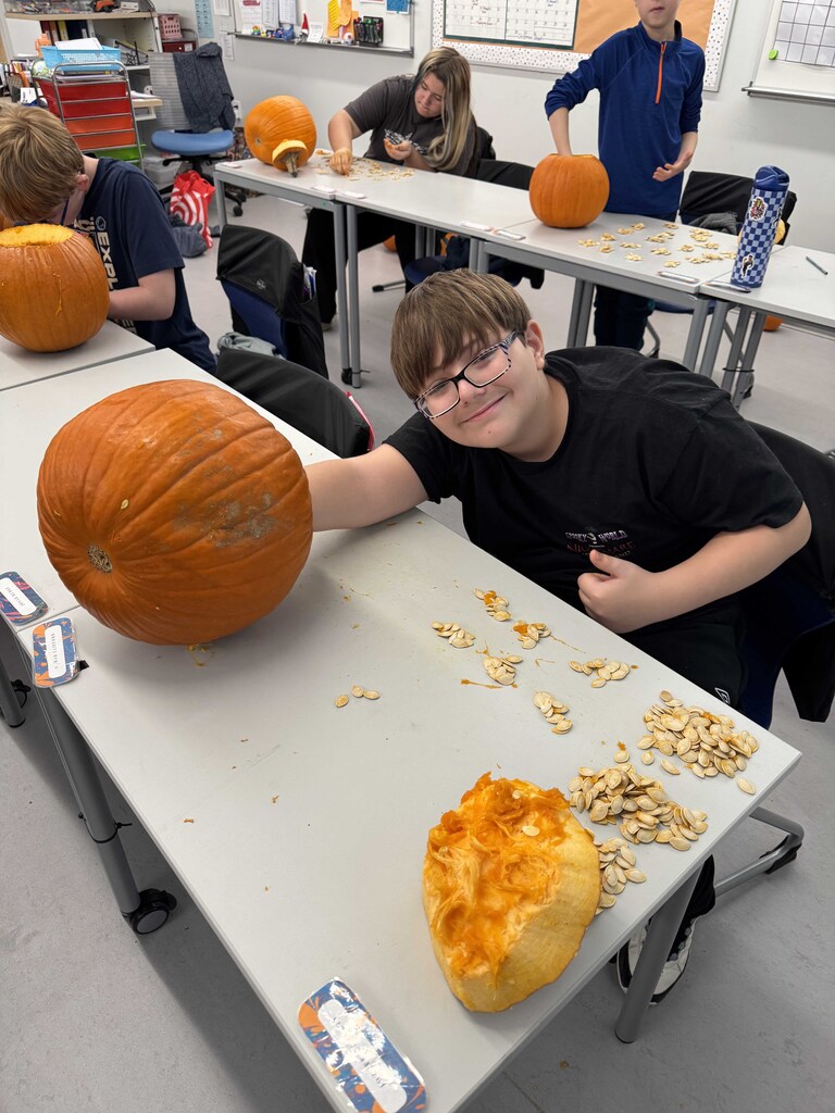 A young man has his hand inside a pumpkin finishing the removal of the insides.