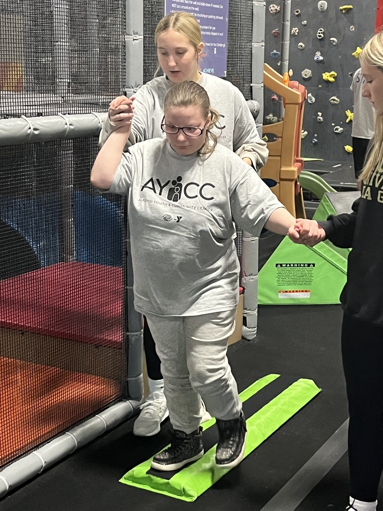 A student is getting assistance from a staff member walking across a bright green balance beam.