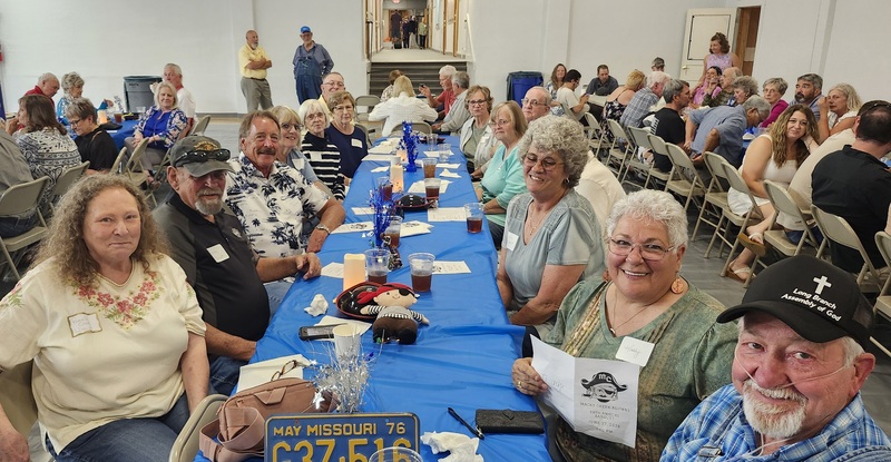 Large group shot of a length of tables with mutiple alumni visiting