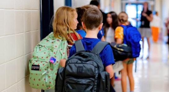 Children in the hallway of a school wearing backpacks in a line. 