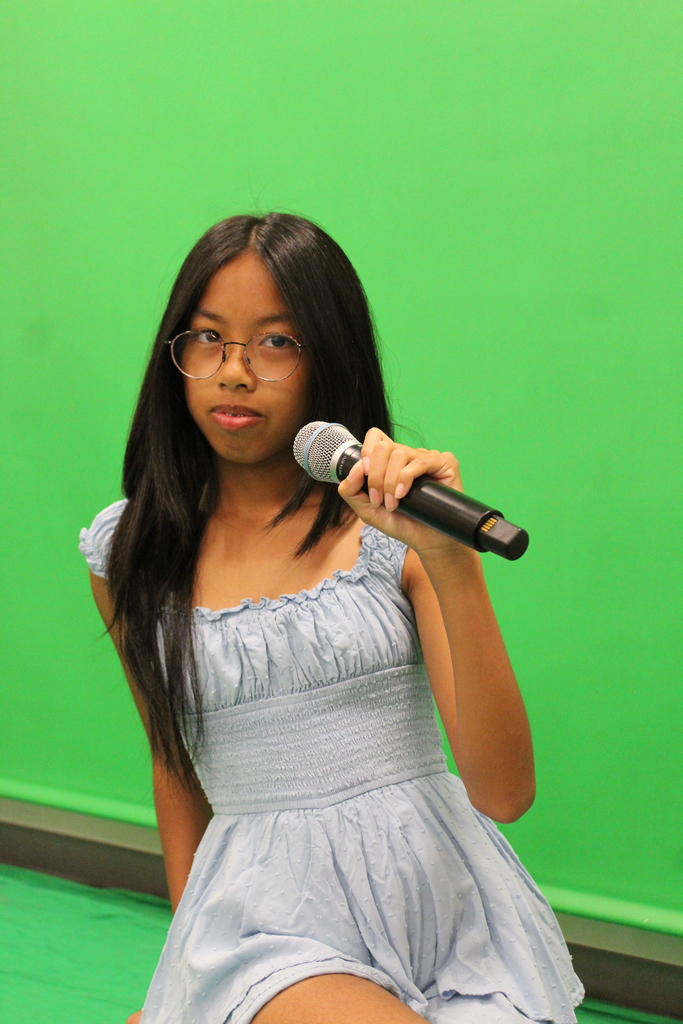 A student with a green screen behind her holding a microphone