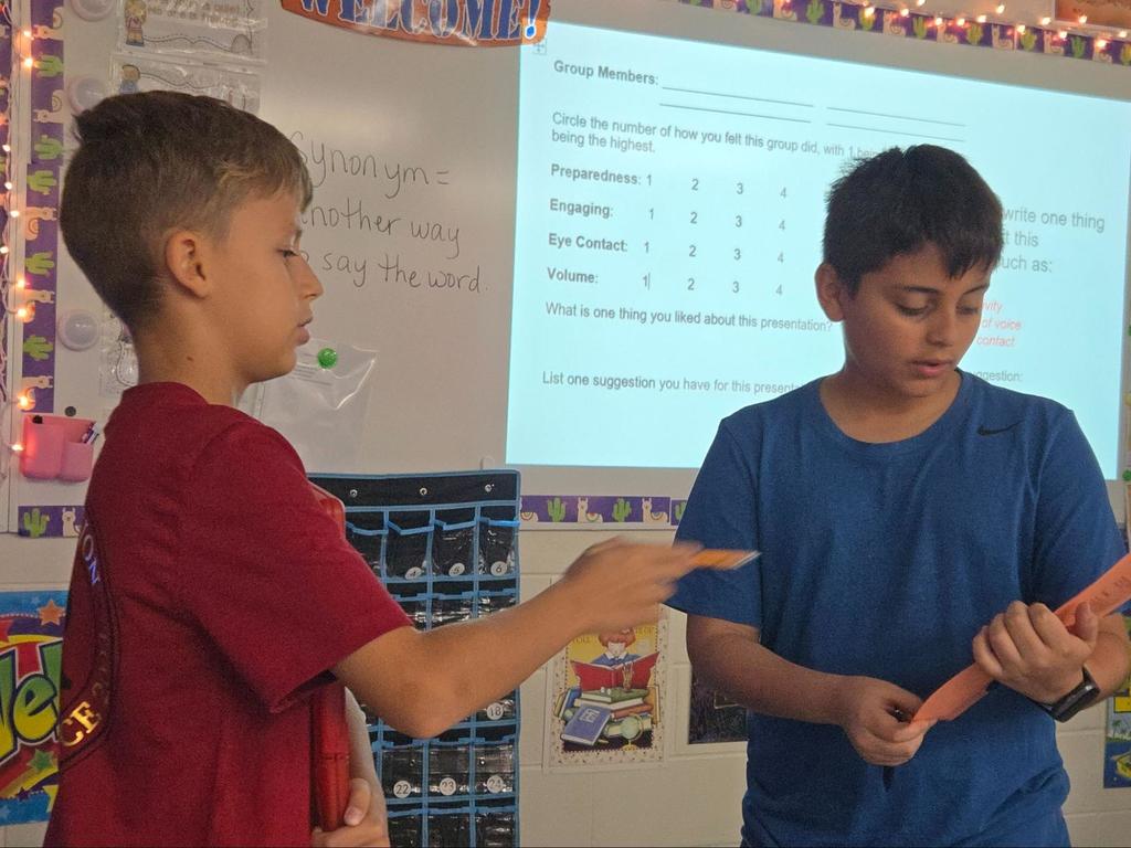 Two boys talking to each other in the classroom with a whiteboard behind them