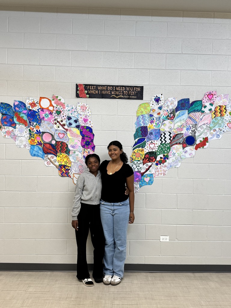 Two students standing in front of an artwork that looks like wings