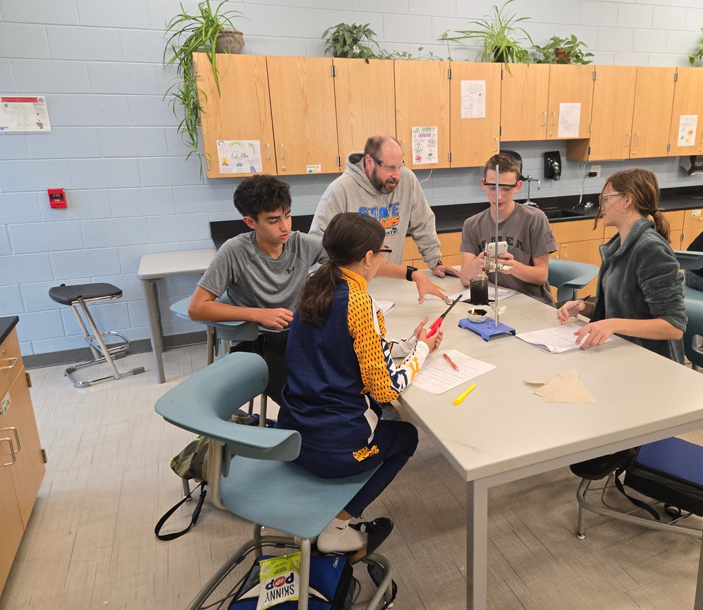 Students work at a table as the teacher helps