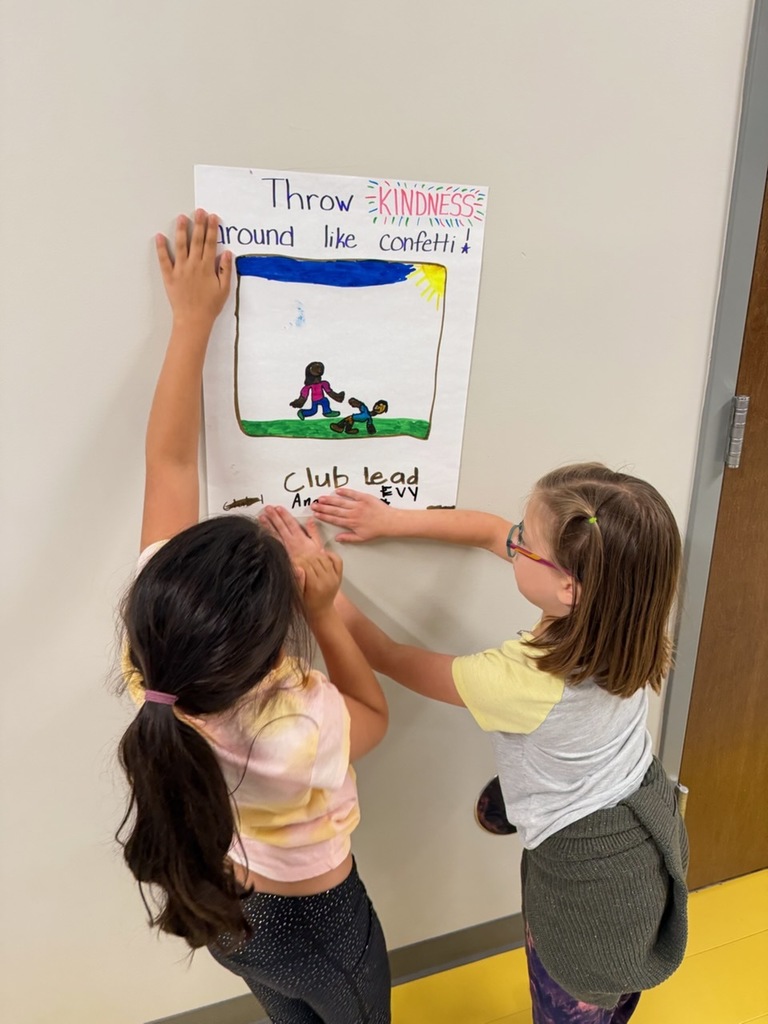 Two students put up a poster that reads "Throw Kindness around the confetti"