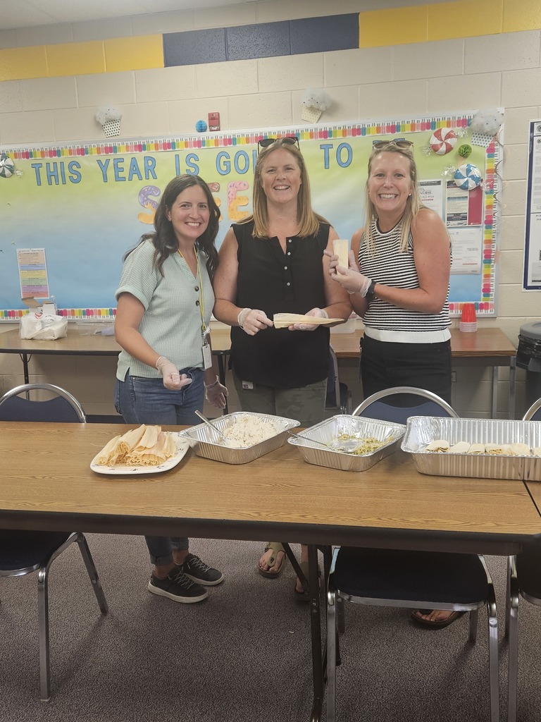 Three staff members smile at the camera while making tamales