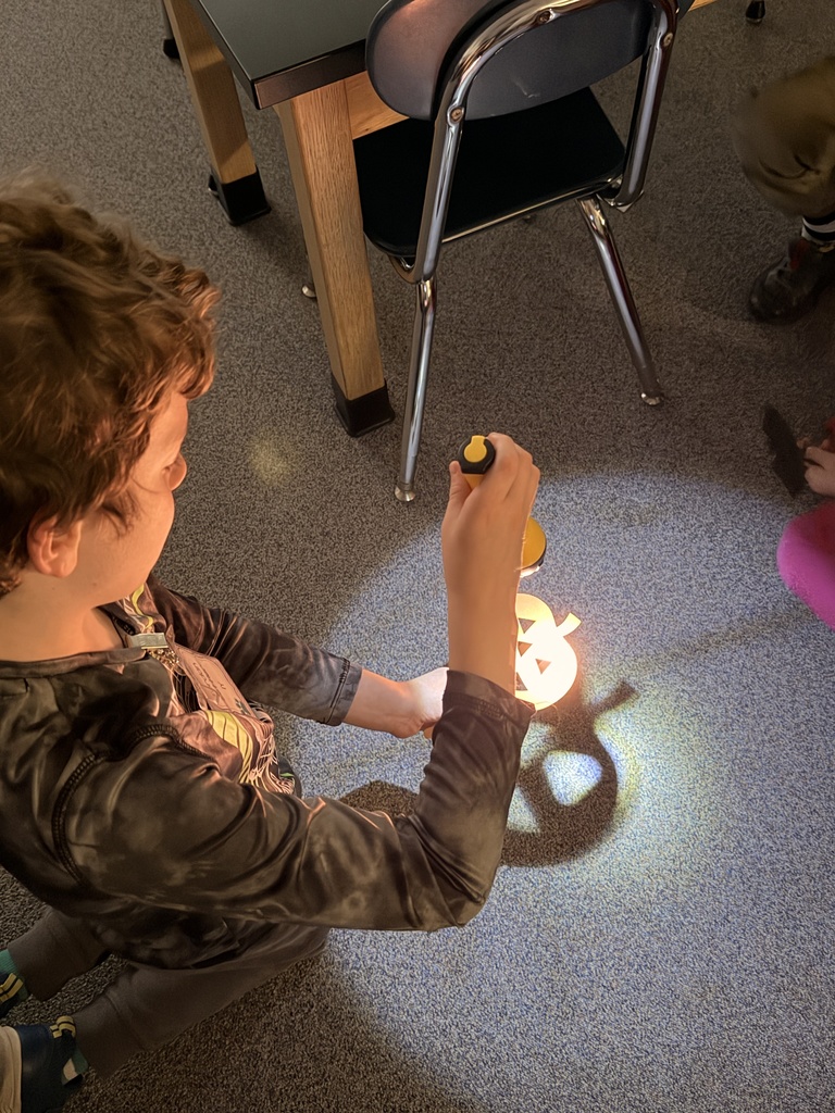 Students make shadows around the room using paper and flashlights