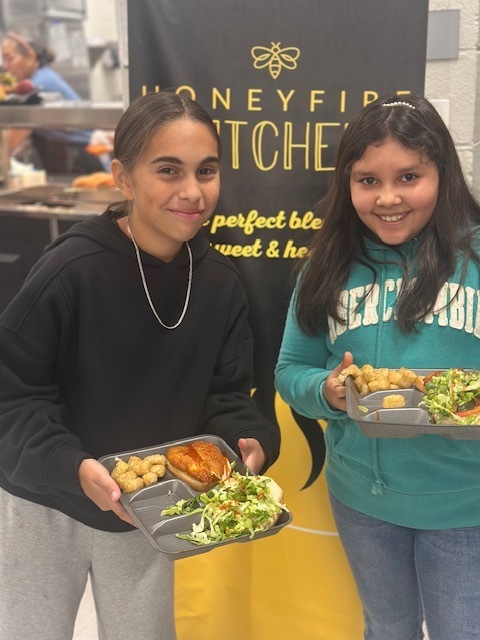 Two students smile at the camera holding plates of food