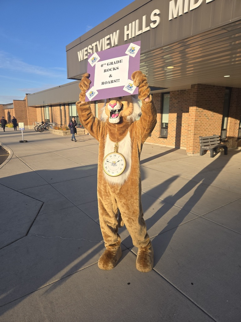 Someone in a lion costume stands outside of Westview Hills holding a sign that says "6th grade rocks and roars!"