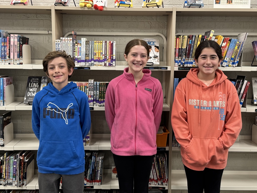 Three students standing in front of books in a library